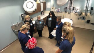 Jennifer Dixon and nurses, wearing scrubs and face masks, hold hands in a circle as they pray