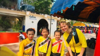 Sierra Drummond, wearing a yellow shirt and black sash, in Thailand posing with three little girls wearing yellow shirts and black, white and red sashes